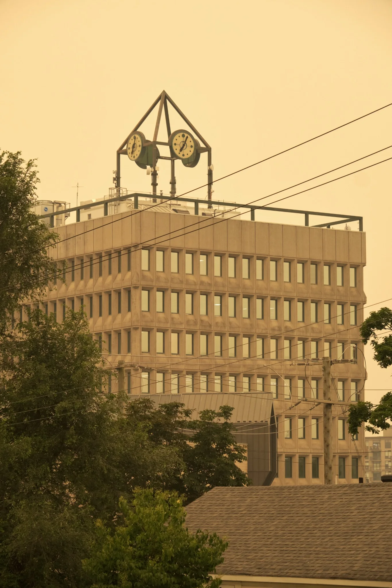 Clock structure rising above a modern civic building under a smoke-filled sky